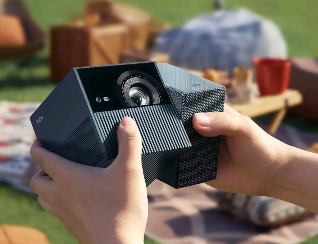 A compact cube projector with twisting hinge, projecting on a wall amid a casual outdoor setting.